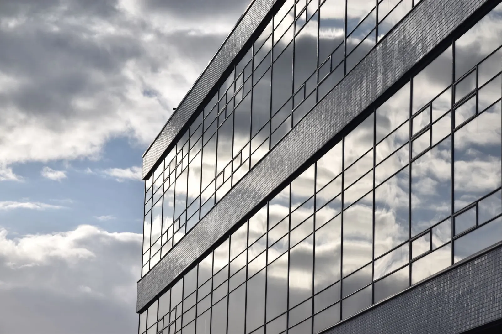 Modern glass office facade reflecting clouds, representing Insika Consulting's professional compliance advisory